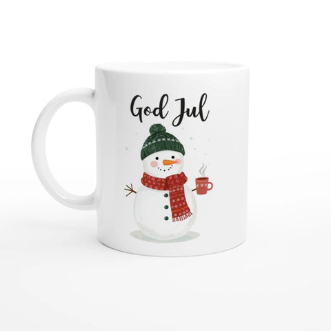 Vit mugg med snögubbe i halsduk och mössa som håller en kopp kaffe och texten “God Jul”