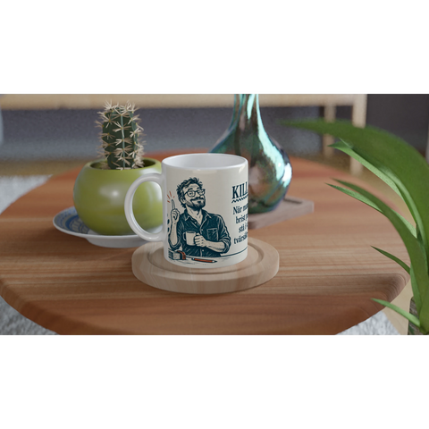 Vit kaffemugg med skämtsamt motiv placerad på ett soffbord