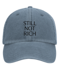 Still Not Rich" svart text på urtvättad blå dad cap, framifrån.