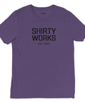 Shirty Works EST. 2025"-tryck i svart på lila triblend t-shirt.