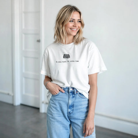 Bokstapel med texten "So many books, so little time" på en vit t-shirt.