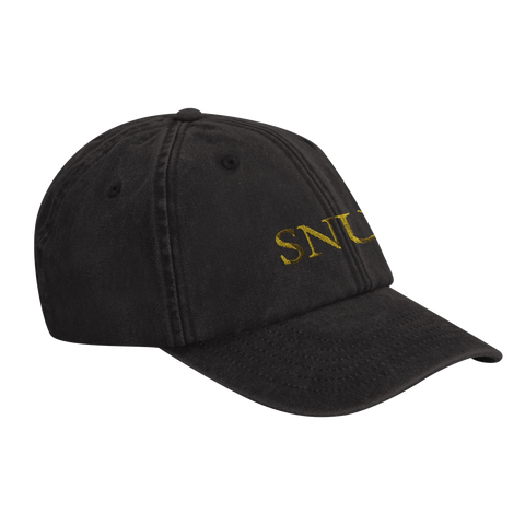 Svart baseballkeps med broderad text i guld. På kepsen står det "SNUS" i guldfärgade bokstäver.
