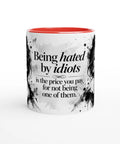 Mugg med texten Being hated by idiots och ett svartvitt kvinnoporträtt.
