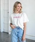 Kvinna bär vit t-shirt med rosa feminist-tryck till blå jeans