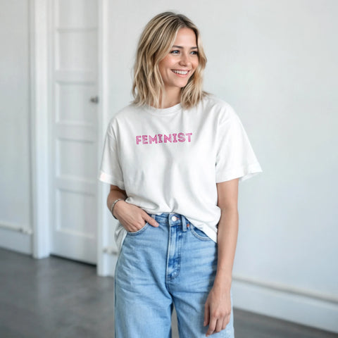 Kvinna bär vit t-shirt med rosa feminist-tryck till blå jeans