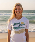 Kvinna bär t-shirt med somrigt kustmotiv vid havet i solnedgång