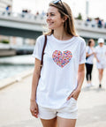 Kvinna bär en vit t-shirt med ett färgglatt hjärtformat tryck utomhus