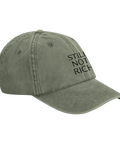 Still Not Rich" text på urtvättad olivgrön dad cap, snett framifrån.