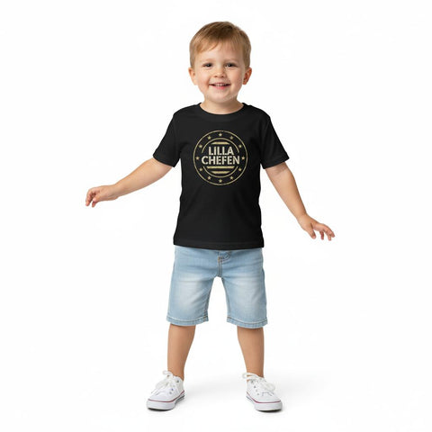 Leende pojke bär en svart t-shirt med det lekfulla motivet Lilla Chefen