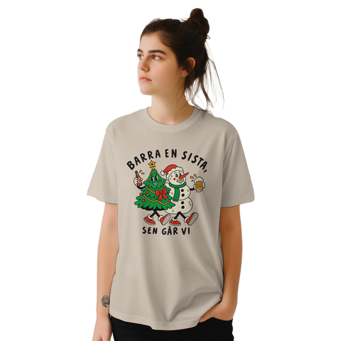 Modell i beige t-shirt med en julgran och snögubbe som skålar och texten ”Barra en sista, sen går vi”.