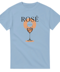 Rosévin i glas med is, orange solnedgång, svart text "ROSÉ" på ljusblå t-shirt.