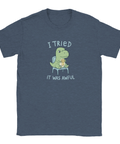Grön dinosaurie med "MEH"-medalj och text "I TRIED IT WAS AWFUL" på marinblå t-shirt.