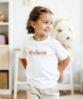 Glad flicka i vit t-shirt med retrotexten Storasyster i ett ljust barnrum