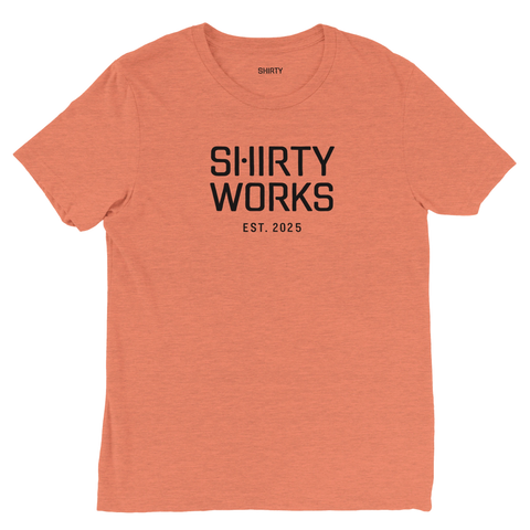 Shirty Works EST. 2025" svart text på persikofärgad triblend t-shirt.