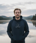 Man i Skitfiske-hook hoodie vid spegelblank sjölandskap.