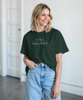 Tre guldkronor och "SVEA RIKE" text på mörkgrön t-shirt, buren av kvinna med ljusa jeans.