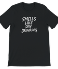 Vit text "SMELLS LIKE DAY DRINKING" med penseldrag på svart t-shirt.