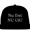 Nu Det NU UK!" broderad i grått på svart snapback-keps, humoristisk stil.