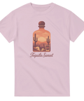 Tequilaflaska med ökensolnedgång, kaktusar, dödskallar, shotglas, text "Tequila Sunset" på rosa t-shirt.
