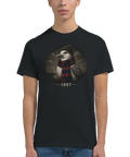 Man bär en svart t-shirt med ett cirkulärt porträtt av en mås och årtalet 1887