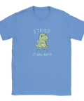 Tecknad dinosaurie med "Meh"-medalj och texten "I tried. It was awful" på ljusblå t-shirt.