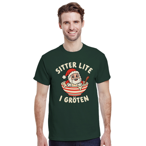 Modell i mörkgrön t-shirt med en tomte i julgröt och texten ”Sitter lite i gröten”.
