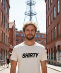 Svart, snedställd "SHIRTY" logotyp med distressed-effekt på en krämvit premium herr-t-shirt.
