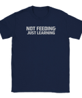NOT FEEDING JUST LEARNING" texttryck i grått på en mörkblå t-shirt.