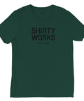 Mörkgrön T-shirt med texten "SHIRTY WORKS EST. 2025" i mörkare gråsvart, minimalistisk stil.