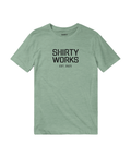 Shirty Works EST. 2025 logga på en grön triblend t-shirt.