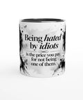 Mugg med texten Being hated by idiots och ett svartvitt kvinnoporträtt.