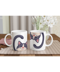 Vit mugg med kattmotiv där en gråvit katt med rosa nos ler gulligt