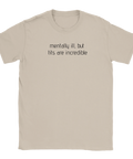Texten "mentally ill, but tits are incredible" i svart på en beige t-shirt, humoristisk design.