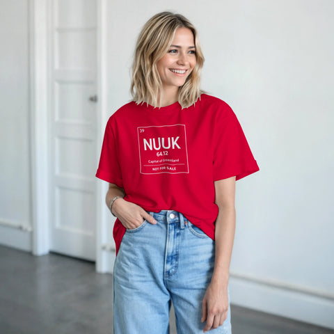 Nuuk periodiskt system-design på röd t-shirt, bärs av leende kvinna i ljusa jeans.