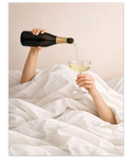 En person häller upp mousserande vin från en flaska i ett coupe-glas under vita krispiga lakan.