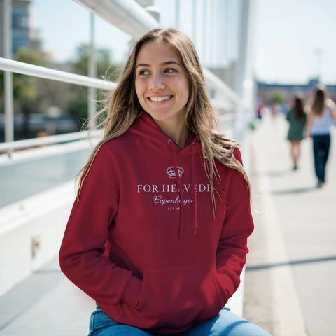Leende kvinna i röd hoodie med vit ”For Helvede Copenhagen”-design.