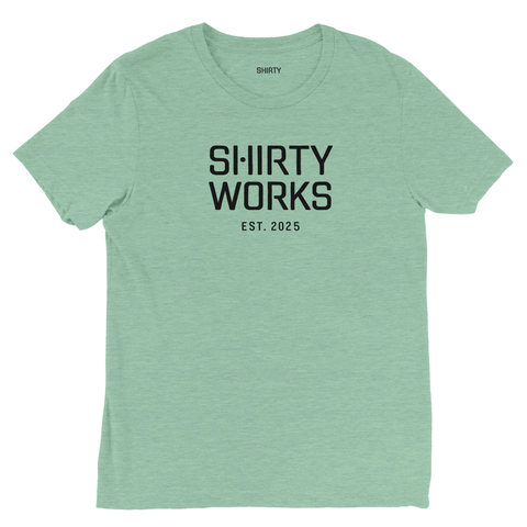 Svart "SHIRTY WORKS EST. 2025" tryck på ljusgrön triblend t-shirt.
