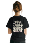 You Are Doing Great" texttryck med bubbliga bokstäver, blommor och smiley på svart t-shirt.