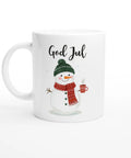 Vit mugg med snögubbe i halsduk och mössa som håller en kopp kaffe och texten “God Jul”