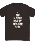 Mörkbrun t-shirt med vit text: "Kaffe först. Frågor sen." och en enkel illustration av en rykande kaffekopp ovanför.
