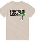 Beige t-shirt med texten "Sportfiske Mode: ON" och illustration av en fiskekrok – perfekt humortröja för sportfiskare